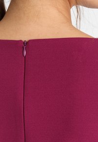 Tajmad plagg i djupt mauve, med dold bakdragkedja och ren halsringning. Slät textur med l ätt lyster.