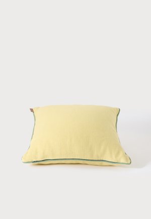 Coussin rectangulaire jaune doux avec un passepoil vert le long des bords sur fond blanc.