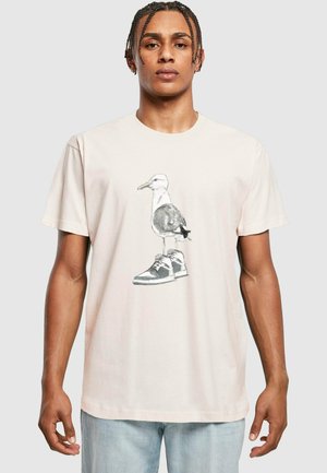 Lys rosa t-skjorte med et grafisk motiv av en fugl som har på seg joggesko. T-skjorten har rund hals og korte ermer, laget av myk bomull.