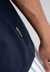 Navy cotton t-shirt featuring a black label with the word "PROHIBITED" in white lettering, visible at the hem, with a textured finish.