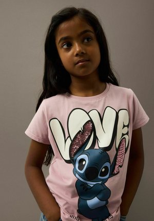 T-shirt en coton rose avec un grand graphisme "LOVE" orné de sequins, affichant un personnage de dessin animé à la peau bleue et aux traits expressifs.