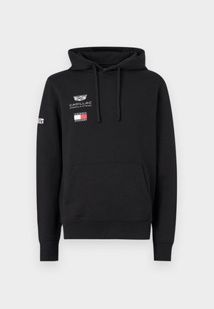 Svart hettegenser med frontlomme, snorer, Cadillac Formula 1 Team- og Tommy Hilfiger-logoer på brystet, og Pirelli-logo på venstre erme.