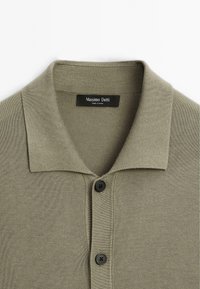 Olivgrön stickad polo med ribbad struktur, platt krage, tre svarta knappar och en etikett som säger "Massimo Dutti."