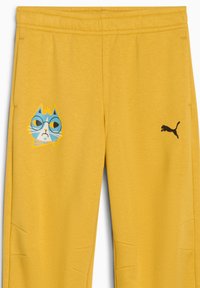 Gule joggers med et blåt kattegrafik iført briller på venstre side og et sort Puma-logo på højre. Blød, bomuldsagtig tekstur.