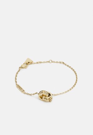 Bracelet doré présentant un motif de crâne au centre, des anneaux entrelacés et un fermoir à mousqueton, avec un design de chaîne texturée et des accents brillants.