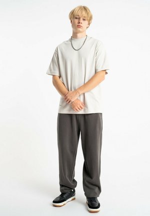 Jasnoszara koszulka z krótkim rękawem o luźnym kroju, zestawiona z ciemnoszarymi spodniami. Czarny buty z białymi podeszwami dopełniają strój.