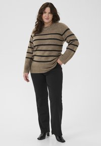 Pull en tricot marron avec des rayures noires, manches larges, ourlet côtelé, associé à un pantalon noir et des bottes à talons noires. Accent d'un collier simple.