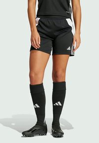 Pantalones cortos deportivos negros con acentos laterales blancos, combinados con calcetas negras hasta la rodilla que presentan una marca blanca y botas negras de diseño aerodinámico.