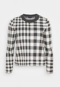 Pull à carreaux noir et blanc avec un col rond côtelé, des manches longues et une coupe ajustée. Le motif présente des carrés et des rayures alternés.