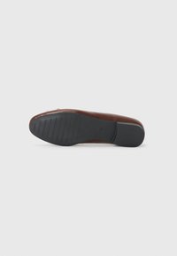 Chaussure plates en cuir marron avec un bout arrondi, dotée d'une semelle en caoutchouc noir texturé et de détails de couture subtils sur le côté.