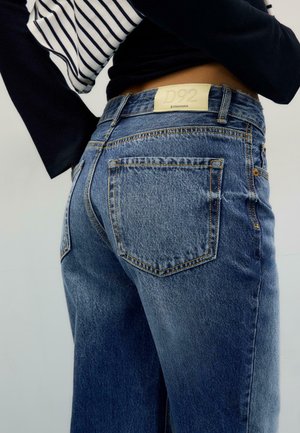 Personne portant un jean en denim bleu taille haute avec une étiquette Stradivarius D92, associé à un haut à manches longues rayé noir et blanc.