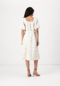 Vestido floral branco com mangas bufantes, costas quadradas e cinto. O tecido apresenta uma estampa botânica colorida, com comprimento até o joelho e uma silhueta fluida.