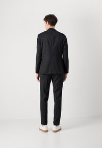 Črn krojen suknjič s strukturo in tesno prilegajoče hlače, v kombinaciji z belimi supergami. Gladka tekstura in minimalističen dizajn.