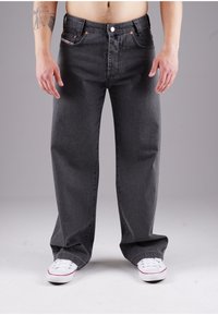 Dark gray denim jeans with a loose fit, five pockets, metal rivets, and copper button closure. Paired with white sneakers.