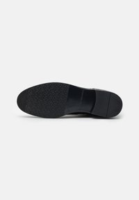 Semelle de chaussure en cuir noir avec un motif de caoutchouc texturé. Présente une surface lisse et un talon arrondi, conçue pour l'adhérence et la durabilité.