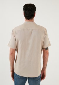 Beige kortemouwen shirt met een subtiele textuur, knoopsluiting kraag en een gebogen zoom, gecombineerd met blauwe denim jeans.