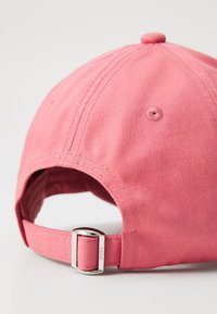 Casquette de baseball rose avec une texture de tissu doux, dotée d'une sangle ajustable et d'un détail de boucle en métal à l'arrière.