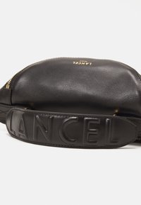 Black leather bag with a smooth texture, featuring a gold logo and a chunky, embossed strap that reads "LANCEL." Zippered closure at the top.
