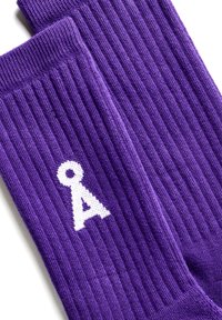 Ein Paar gerippte lila Socken mit einem weißen stilisierten schlüsselförmigen Symbol auf einer Socke vor einem weißen Hintergrund.