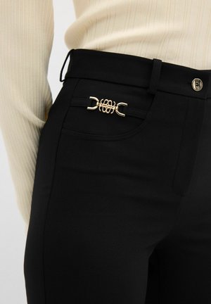 Schwarze hoch taillierte Hose mit einem goldenen dekorativen Verschluss an der Vorderseite, aus einem glatten Stoff mit tailliertem Schnitt.