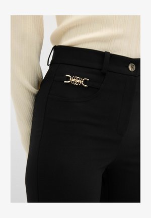 Schwarze hoch taillierte Hose mit einem goldenen dekorativen Verschluss an der Vorderseite, aus einem glatten Stoff mit tailliertem Schnitt.