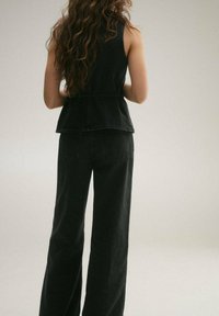 Črna jeansa peplum majica v kombinaciji z visokim pasom, širokimi črnimi hlačami. Material se zdi trden, z gladko teksturo in minimalnim šivom.