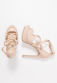 Beige hoge haksandalen met kruislings strapjes, spitse neus en een platform basis; glanzende leren afwerking met een dunne stilettohak.