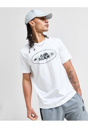 Giovane uomo con t-shirt bianca Nike Air Max e cappellino grigio chiaro guarda verso destra, con dreadlocks a quattro ciocche e tatuaggio sull'avambraccio sinistro.