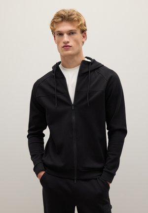 Sudadera con cremallera negra, capucha con cordones, tejido suave, dos bolsillos frontales y un diseño ajustado. Presenta una textura lisa y un detalle mínimo.