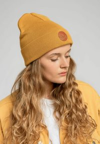 Musztardowa żółta dziana czapka beanie o prążkowanej fakturze i okrągłej skórzanej łatce. Dopasowana, z lekkim szpicem na czubku.