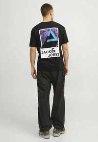 T-shirt nero a maniche corte con una grande grafica viola e blu con il testo "JACK & JONES" sul retro. Abbinato a pantaloni larghi scuri.
