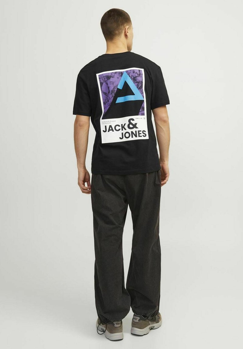 T-shirt nero a maniche corte con una grande grafica viola e blu con il testo "JACK & JONES" sul retro. Abbinato a pantaloni larghi scuri.