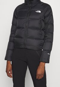 Veste doudoune noire au design court, fermeture à glissière sur le devant, poignets côtelés et accents de logo. Fabriquée en tissu lisse et isolant.