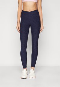 Mørkeblå leggings med melert tekstur, høy midje og tettsittende design, sammen med hvite treningssko.