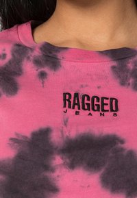 Pink tie-dye t-shirt with black accents and ribbed neckline, featuring the embroidered text "RAGGED JEANS" in black.