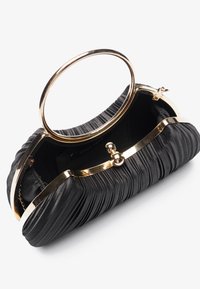 Sac à main plissé noir avec un cadre en métal doré et une poignée circulaire. L'intérieur est doublé de tissu noir et comporte un fermoir.