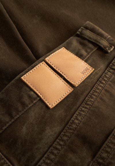 Material maro din catifea cu o suprafață texturată, cu două petice dreptunghiulare din piele de culoare bronz, cusute pe talie.