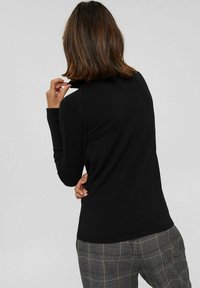 Zwarte gebreide trui met een hoge kraag en lange mouwen, voorzien van geribbelde manchetten en zoom, gecombineerd met geruite stoffen broek.