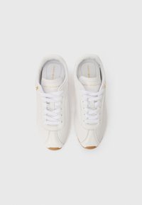 Λευκά αθλητικά παπούτσια φτιαγμένα από δέρμα, με στρογγυλή μύτη, περφοραρισμένες λεπτομέρειες, λαστιχένια κορδόνια και καουτσούκ σόλα με καφέ λεπτομέρεια.