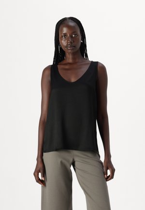 Top negru fără mâneci cu un design în formă de V, realizat dintr-un material neted. Croiala este lejeră, asortată cu o pereche de pantaloni largi gri deschis.