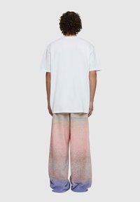 Bijela oversized majica kratkih rukava u kombinaciji s hlačama visokog struka širokih nogavica koje imaju gradijent od ružičaste do plave boje s teksturiranim završetkom.