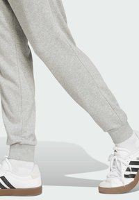 Svijetlosivi trenirci s rebrastim manžetama, upareni s bijelim tenisicama koje imaju tri crne pruge i smeđu gumenu podlogu.