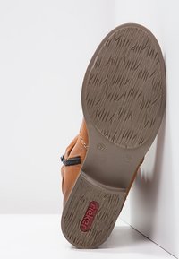 Botte de cheville en cuir marron avec une semelle texturée, fermeture éclair latérale et détail de logo rouge. Présente une pointe arrondie et de subtils accents de couture.