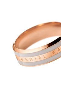 Kullanışlı modern tasarıma sahip, beyaz seramik inlaylarla süslenmiş altın tonlu paslanmaz çelik yüzük; "DANIEL WELLINGTON" yazılı. 