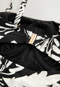 Čiernobiely kvetinový vrchný diel bikín s tenkými nastaviteľnými ramienkami a zlatým zapínaním v strede prednej časti.