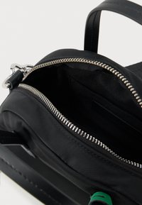 Μαύρη νάιλον τσάντα με ασημί φερμουάρ, εσωτερικές τσέπες και μαύρη επένδυση υφάσματος. Ορατό πράσινο στοιχείο στο εσωτερικό.