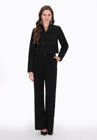 Costum negru, adaptat, care prezintă o jachetă scurtă, cu rever dublu și nasturi în formă de inimă, împreună cu pantaloni evazați. Material neted, design elegant.