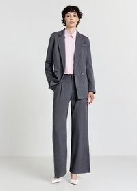 Blazer à rayures grises et pantalon large associé à une chemise rose à col. Des escarpins blancs à bout pointu complètent le look. Texture lisse.