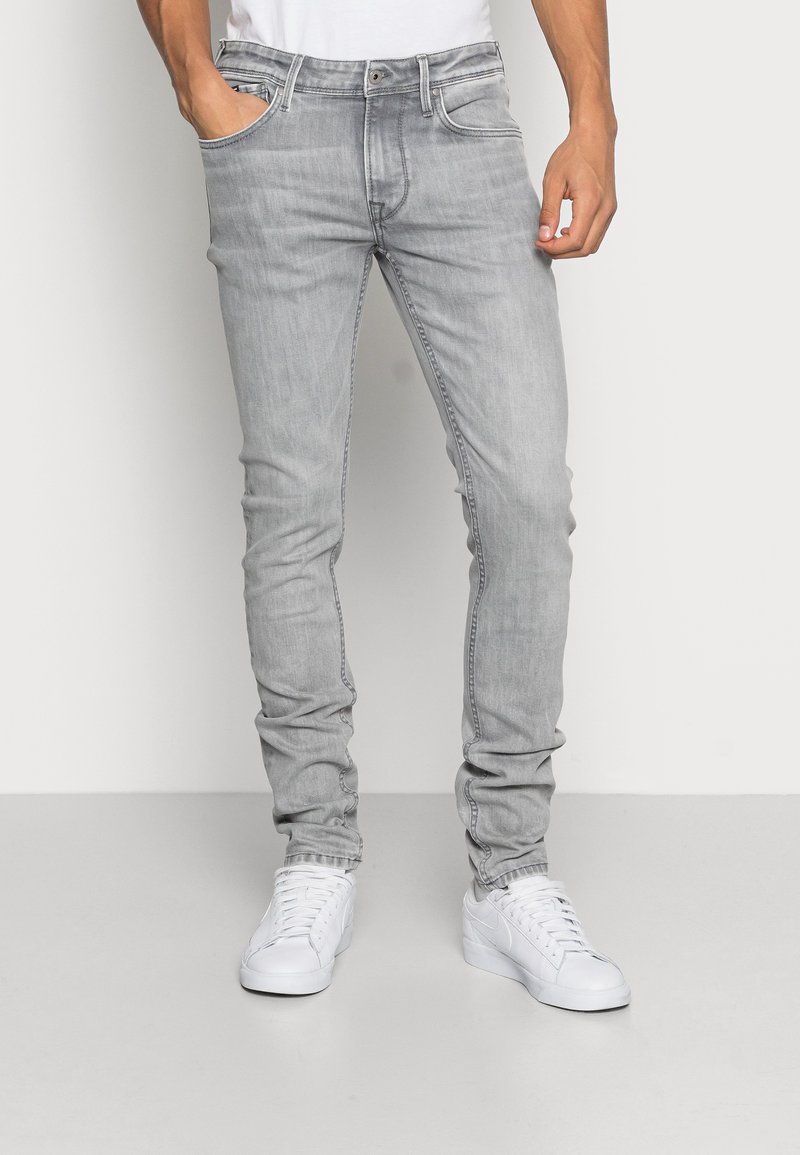 Szürke slim-fit farmer, sima denim textúrával, öt zsebes dizájnnal és diszkrét kopással, fehér sportcipővel és sima fehér pólóval párosítva.