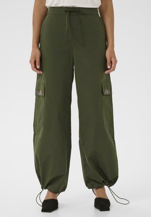 Olivgrüne Cargo-Hosen mit Kordelzug am Saum und gestickten Taschenklappen, getragen mit schwarzen spitzen Schuhen und einem weißen Oberteil.